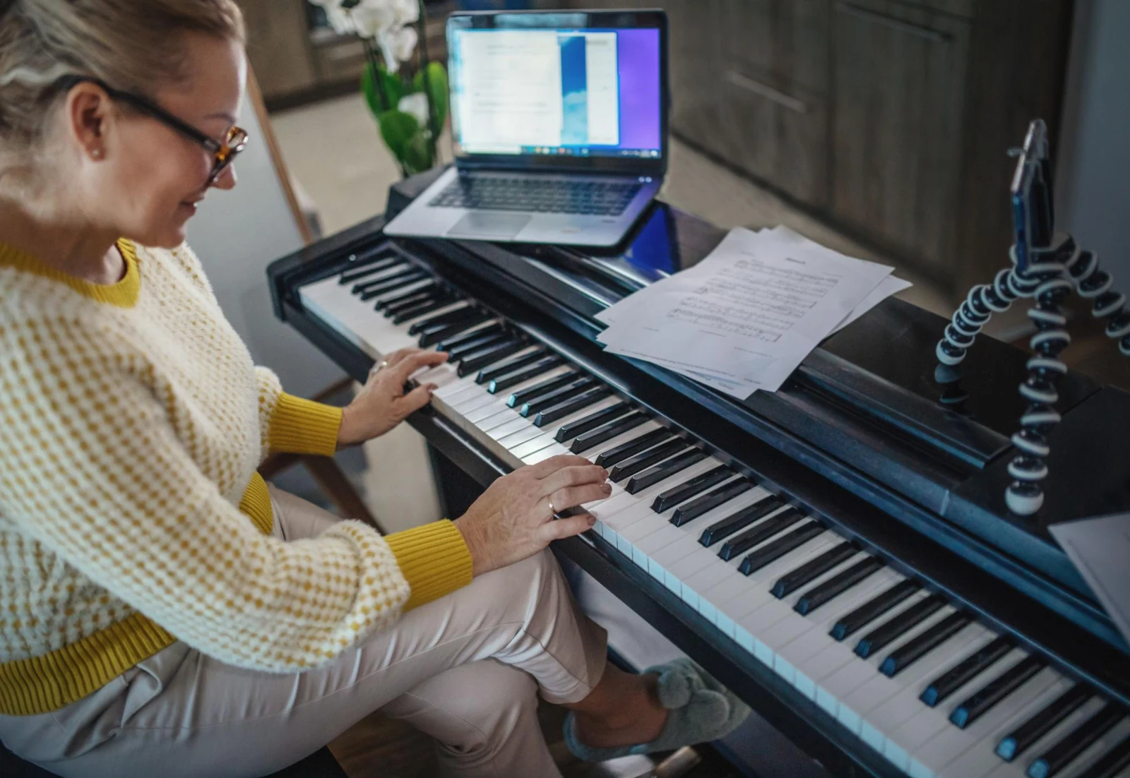 Adult learner playing a digital piano at home with a laptop set up for an online lesson.