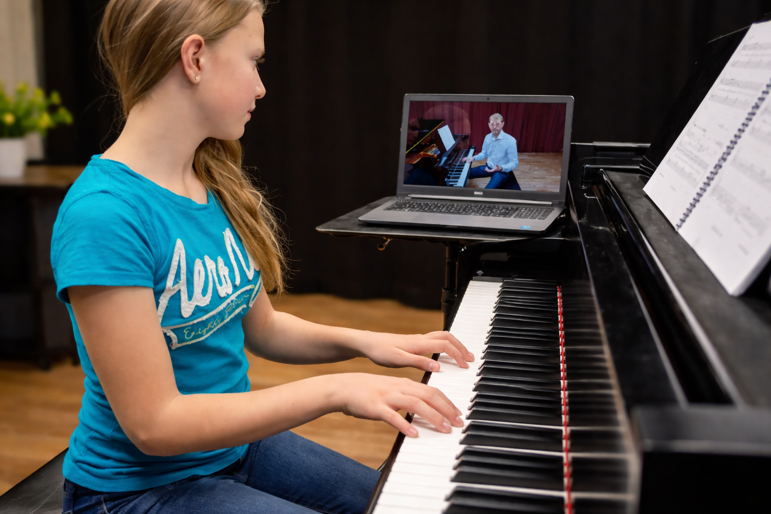 Student taking an online piano lesson using a laptop at a piano